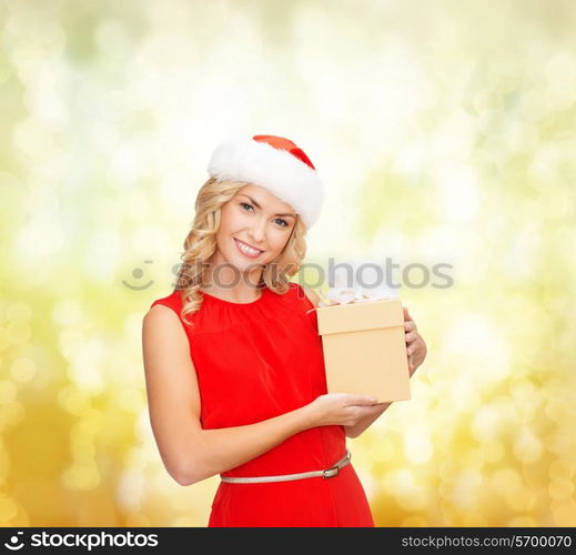 christmas, winter, happiness, holidays and people concept- smiling woman in santa helper hat with gift box over yellow lights background