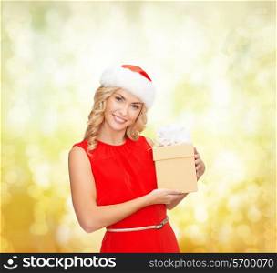 christmas, winter, happiness, holidays and people concept- smiling woman in santa helper hat with gift box over yellow lights background