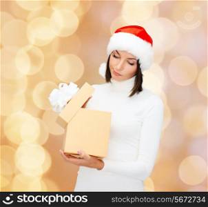 christmas, winter, happiness, holidays and people concept - woman in santa helper hat with gift box over beige lights background