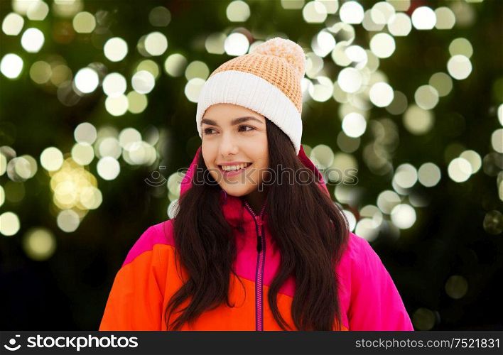 christmas, winter holiday and people concept - happy young woman over festive lights on dark green background. happy young woman in winter clothes outdoors