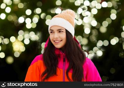 christmas, winter holiday and people concept - happy young woman over festive lights on dark green background. happy young woman in winter clothes outdoors