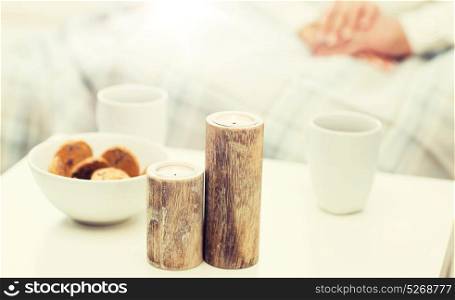 christmas, winter, holidays and concept - close up of candles, cookies and tea cups on table over family couple on background. close up of candles, cookies and tea cups on table