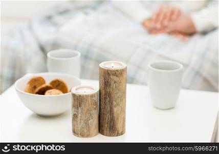 christmas, winter, holidays and concept - close up of candles, cookies and tea cups on table over family couple on background