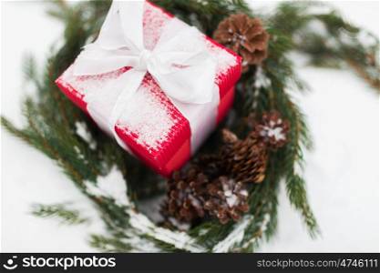 christmas, winter holidays and greeting concept - close up of gift box and fir wreath with cones on snow