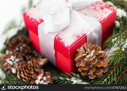 christmas, winter holidays and greeting concept - close up of gift box and fir wreath with cones on snow