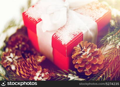 christmas, winter holidays and greeting concept - close up of gift box and fir wreath with cones on snow. close up of christmas gift and fir wreath on snow