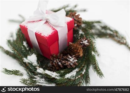 christmas, winter holidays and greeting concept - gift box and fir wreath with cones on snow