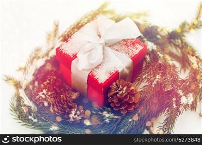 christmas, winter holidays and greeting concept - gift box and fir wreath with cones on snow. christmas gift and fir wreath with cones on snow