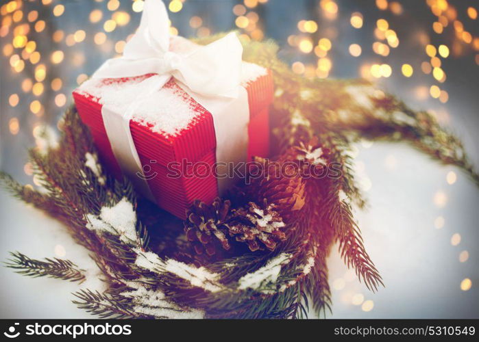 christmas, winter holidays and greeting concept - gift box and fir wreath with cones on snow. christmas gift and fir wreath with cones on snow