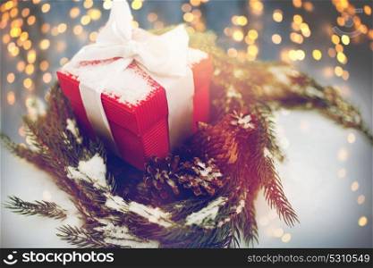 christmas, winter holidays and greeting concept - gift box and fir wreath with cones on snow. christmas gift and fir wreath with cones on snow