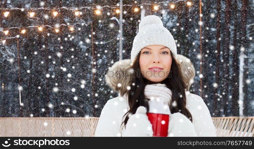 christmas, winter holidays and leisure concept - happy young woman with tea cup over ice skating rink on background. woman with tea cup at ice skating rink in winter