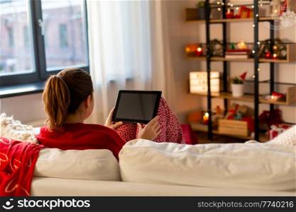 christmas, winter holidays and leisure concept - young woman with tablet pc computer sitting on sofa at home. woman with tablet computer at home on christmas