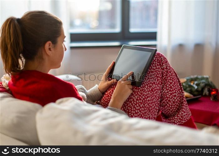 christmas, winter holidays and leisure concept - young woman with tablet pc computer sitting on sofa at home. woman with tablet computer at home on christmas
