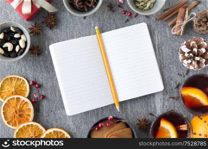 christmas, winter holidays and new start concept - notebook with pencil, hot mulled wine and aromatic spices on grey background. notebook, pencil and hot mulled wine on christmas
