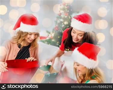 christmas, winter, holidays and people concept - happy women in santa hats with gifts in shopping bags over lights background