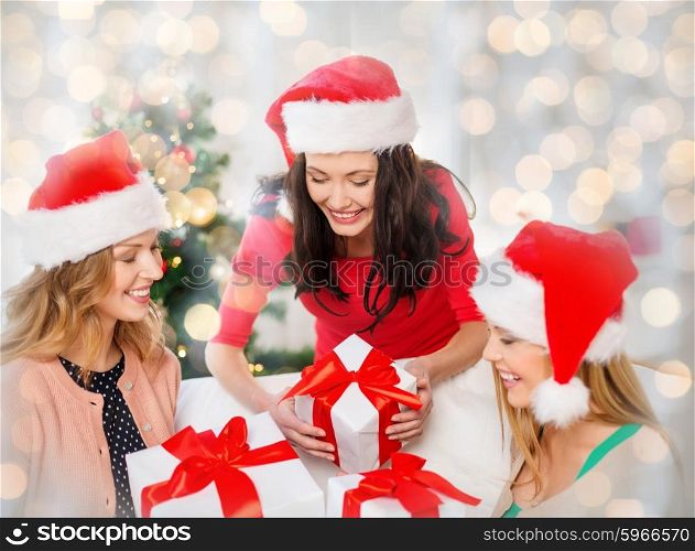 christmas, winter, holidays and people concept - happy women in santa hats with gift boxes over lights background