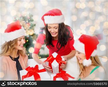 christmas, winter, holidays and people concept - happy women in santa hats with gift boxes over lights background