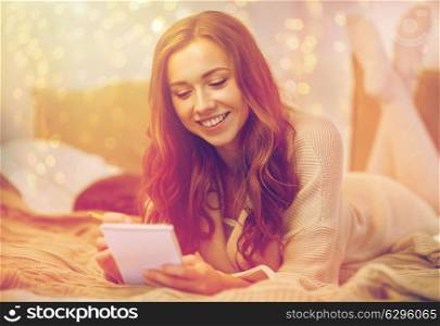 christmas, winter, holidays and people concept - happy young woman with pencil and notebook writing in bed at home bedroom. happy young woman with notebook in bed at home