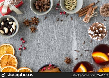 christmas, winter holidays and seasonal drinks concept - hot mulled wine, dry orange slices, raisins with pine cones and aromatic spices on grey background. hot mulled wine, orange slices, raisins and spices