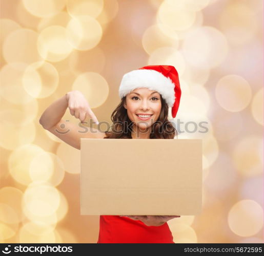 christmas, winter, holidays, delivery and people concept - smiling woman in santa helper hat with parcel box over beige lights background