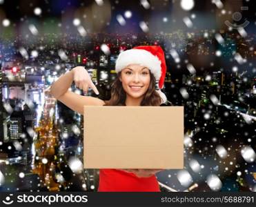 christmas, winter, holidays, delivery and people concept - smiling woman in santa helper hat with parcel box over snowy night city background