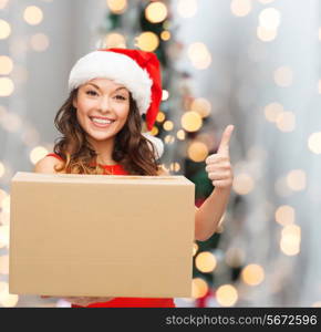 christmas, winter holidays, delivery, gesture and people concept - smiling woman in santa helper hat with parcel box showing thumbs up over living room with christmas tree background
