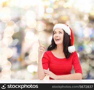 christmas, winter, holidays, happiness and people concept - smiling woman in santa helper hat pointing finger over lights background