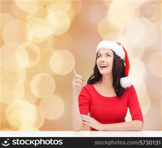 christmas, winter, holidays, happiness and people concept - smiling woman in santa helper hat pointing finger over beige lights background