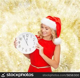 christmas, winter, holidays, time and people concept - smiling woman in santa helper hat and red dress with clock over yellow lights background
