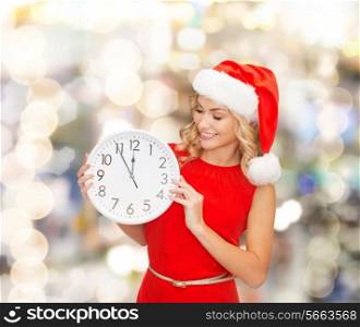 christmas, winter, holidays, time and people concept - smiling woman in santa helper hat and red dress with clock over lights background