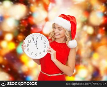 christmas, winter, holidays, time and people concept - smiling woman in santa helper hat and red dress with clock over red lights background