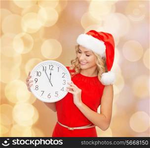 christmas, winter, holidays, time and people concept - smiling woman in santa helper hat and red dress with clock over beige lights background