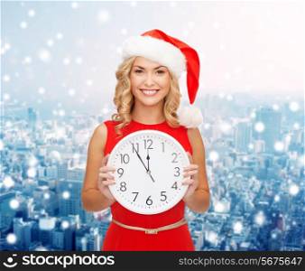 christmas, winter, holidays, time and people concept - smiling woman in santa helper hat and red dress with clock over snowy city background