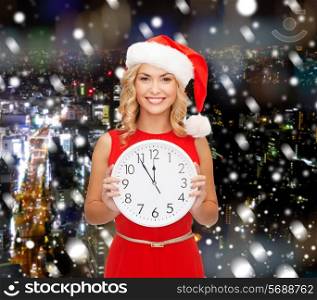 christmas, winter, holidays, time and people concept - smiling woman in santa helper hat and red dress with clock over snowy city background