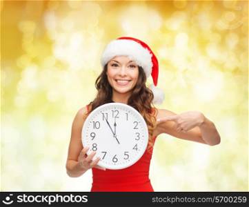 christmas, winter, holidays, time and people concept - smiling woman in santa helper hat and red dress with clock over yellow lights background