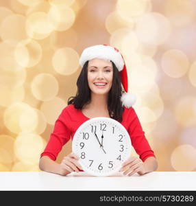 christmas, winter, holidays, time and people concept - smiling woman in santa helper hat and red dress with clock over beige lights background