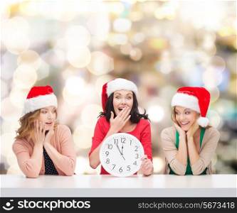 christmas, winter, holidays, time and people concept - smiling women in santa helper hats with clock over lights background