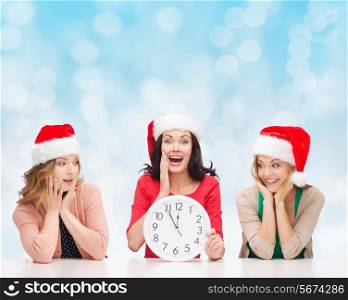 christmas, winter, holidays, time and people concept - smiling women in santa helper hats with clock over blue lights background
