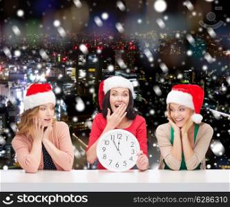 christmas, winter, holidays, time and people concept - smiling women in santa helper hats with clock over snowy night city background