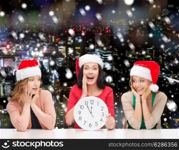 christmas, winter, holidays, time and people concept - smiling women in santa helper hats with clock over snowy night city background