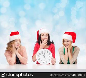 christmas, winter, holidays, time and people concept - smiling women in santa helper hats with clock over blue lights background