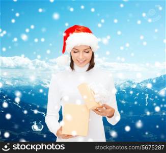 christmas, winter, travel, holidays and people concept - smiling woman in santa helper hat opening gift box over snowy mountains background