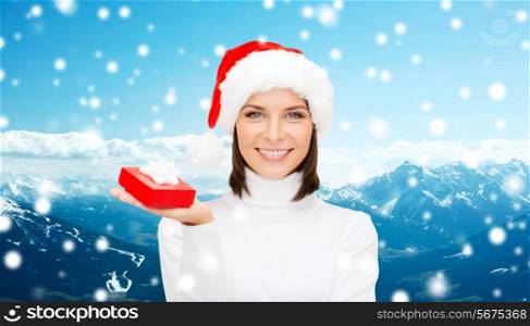 christmas, winter, travel, holidays and people concept - smiling woman in santa helper hat with small red gift box over snowy mountains background