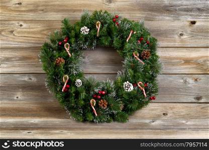 Christmas wreath decorated with pine cones, candy canes, and red berries on rustic wooden boards.
