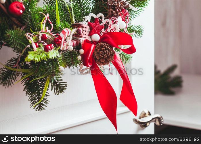 Christmas wreath hangs on the white doors. Red and white elements, bow for decorating holiday house. Red and white Christmas wreath