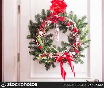 Christmas wreath hangs on the white doors. Red and white elements, bow for decorating holiday house. Red and white Christmas wreath
