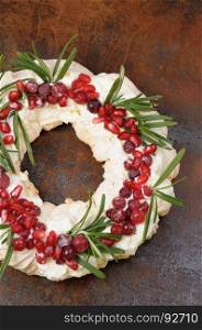 Christmas wreath made of meringue with cream, pomegranate, cranberry, rosemary closeup