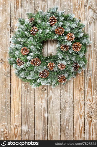 Christmas wreath on rustic wooden background. Christmas decoration with falling snow effect