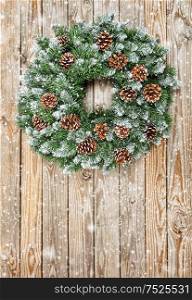 Christmas wreath on rustic wooden background. Christmas decoration with falling snow effect