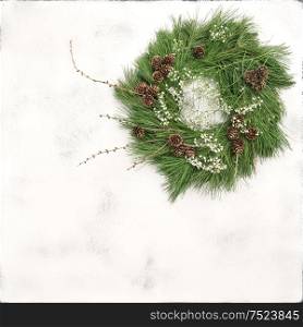 Christmas wreath with pine cones and white flowers on bright stone background